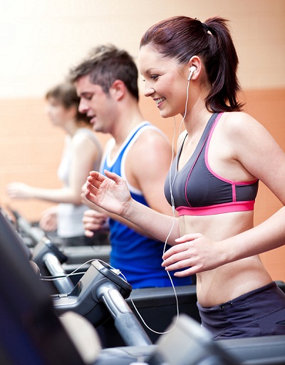 Beautiful female athlete standing on a running machine listening